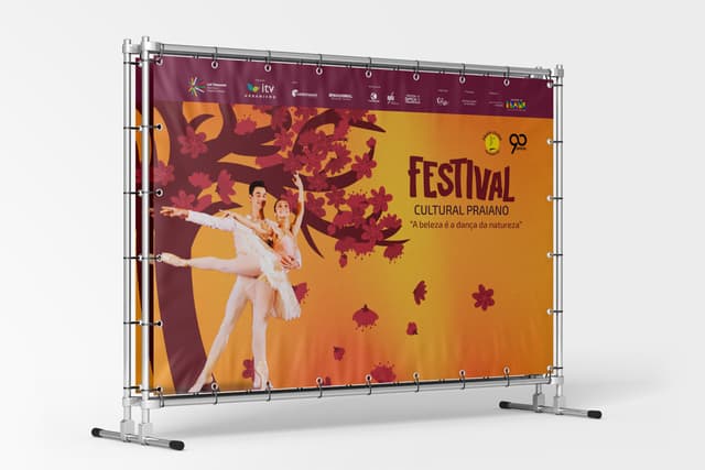 Backdrop do Festival Cultural Praiano montado em estrutura de metal, com casal de bailarinos e árvore de flores sobre fundo laranja